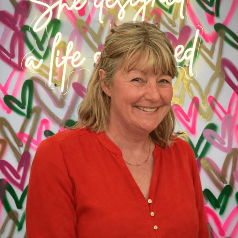 Woman in a red shirt standing in front of a colorful, abstract wall with text.
